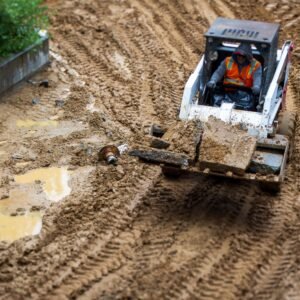 A worker operates a backhoe in a muddy construction site, showcasing heavy machinery in action.