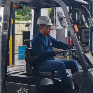An industrial worker wearing protective gear operates a forklift inside a warehouse.